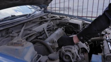 Beyaz adam arabadaki bujileri değiştiriyor.