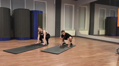 İki beyaz kadın spor salonunda burpee yapıyor.
