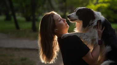 Beyaz bir kadın parkta yürürken köpeğine sarılıyor.
