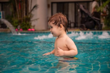 Bir yaşında beyaz çocuk yüzme havuzunda top oynuyor.