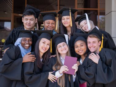 Farklı uluslardan mutlu öğrenciler mezuniyet elbiseleriyle diplomalarını tutuyorlar.