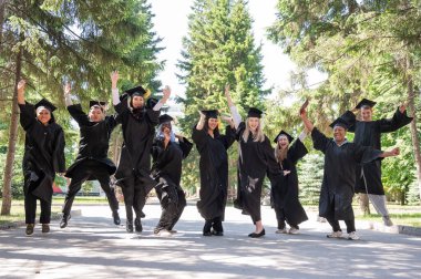 Mezuniyet elbiseleriyle dışarıda neşe içinde zıplayan çok uluslu gençler.