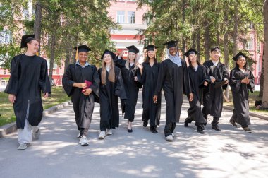 Mezuniyet elbisesi giyen farklı uluslardan öğrenciler kampüste yürüyorlar.