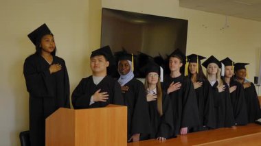 Mezunlar törende gururla dururlar. Elleri kalplerinin üstünde.