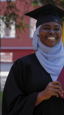 Tesettürlü mutlu Afrikalı kadın diploma alıyor ve sınıf arkadaşları onu alkışlıyor.