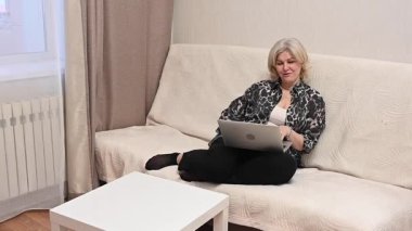 Kanepede otururken laptop kullanan olgun bir kadın.