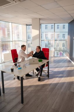 Bir ofiste sohbet eden iki beyaz adam.