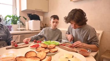 Orta yaşlı beyaz kadın iki oğluyla hamburger pişiriyor.