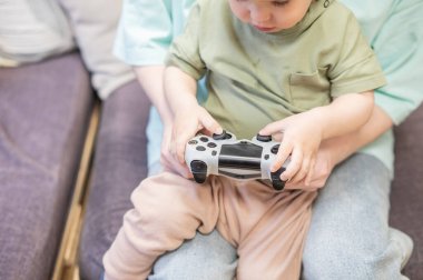 Beyaz kadın küçük oğluna konsol oynamayı öğretiyor. Oyun kolu ellerinde.