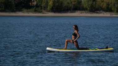 Beyaz kadın SUP panosunda yoga yapıyor.