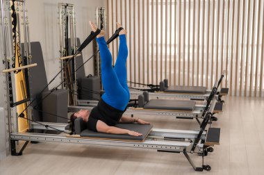 Aşırı kilolu beyaz kadın bir reformcu üzerinde pilates egzersizi yapıyor.