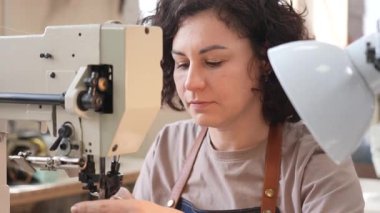 Bir kadın tabakçı dikiş makinesine deri kemer dikiyor.