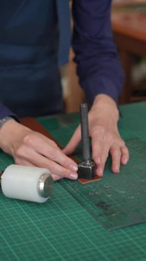 Deri işçisi bir atölyedeki kemerden bir parça deri kesiyor.