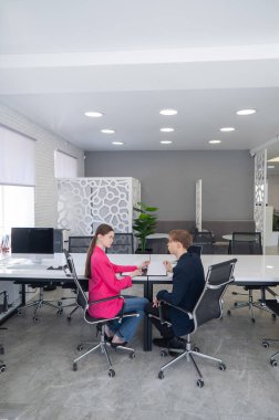 Kadın ve erkek ofiste otururken konuşuyorlar.