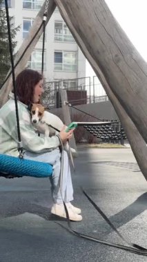 Beyaz kadın Jack Russell Terrier 'ını gezdirirken akıllı telefon kullanıyor.