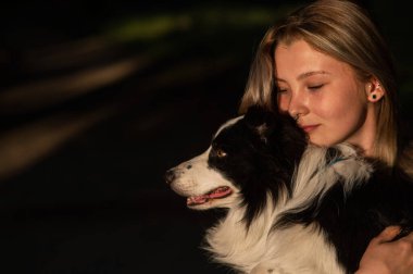 Beyaz bir kadın parkta yürürken köpeğine sarılıyor.