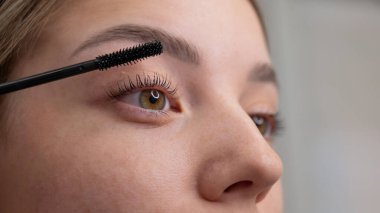 Genç bir kadının dikkatlice maskarasını kirpiklerine sürerken.