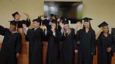 Mezuniyet elbisesi giymiş farklı uluslardan öğrenciler ellerini sallıyor.