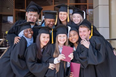 Farklı uluslardan mutlu öğrenciler mezuniyet elbiseleriyle diplomalarını tutuyorlar.
