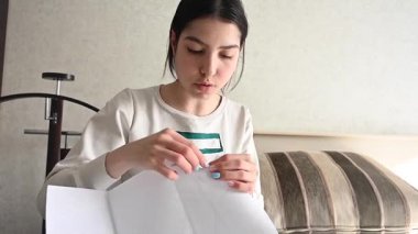 Genç beyaz kadın yatakta otururken çapraz dikiş atıyor.