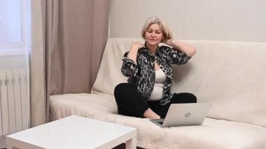 Kanepede otururken laptop kullanan olgun bir kadın.