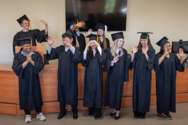 Mezuniyet elbisesi giymiş çok uluslu genç insanlar kürsüde duruyorlar.