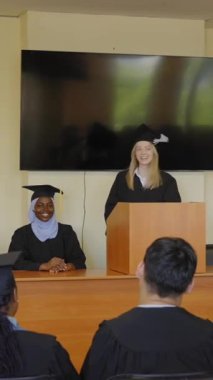 Genç bir kadın kürsüde duruyor ve sınıf arkadaşlarına mezuniyet konuşması yapıyor.