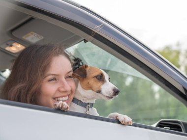 Beyaz kadın köpekle birlikte arabanın camından dışarı bakıyor.