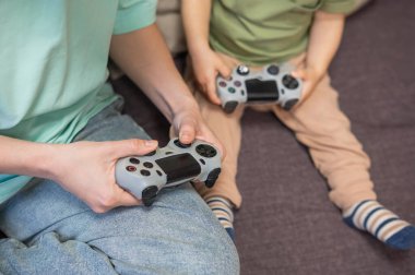 Beyaz kadın küçük oğluna konsol oynamayı öğretiyor. Oyun kolu ellerinde.