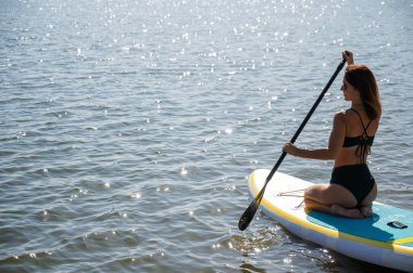Güzel beyaz kadın SUP tahtasının üzerinde yüzüyor.