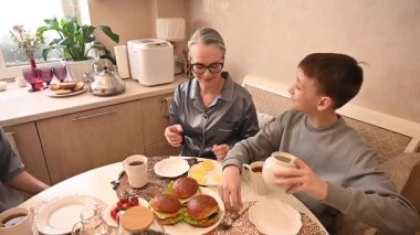 Orta yaşlı beyaz bir kadın iki oğluyla yemek yiyor. Aile çay partisi.