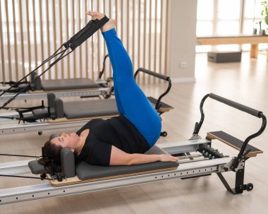Aşırı kilolu beyaz kadın bir reformcu üzerinde pilates egzersizi yapıyor.