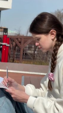 Açık havada kalemle çizim yapan beyaz bir kadın.