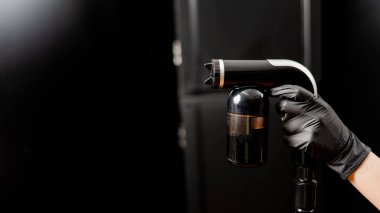 Bir ustanın ellerinde hazır bronzlaşma ekipmanlarının yakın çekimi. Siyah arka plana karşı deri boya sıkmak..