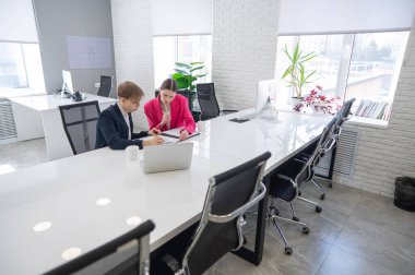 Kadın ve erkek ofiste otururken konuşuyorlar.