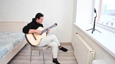 Genç adam kendini akıllı telefondan çekerken akustik gitar çalıyor. Parmak Biçimi
