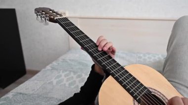 Genç bir adam yatakta akustik gitar çalıyor. Parmak Biçimi