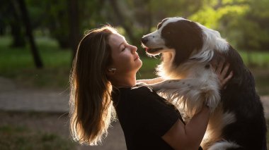 Beyaz bir kadın parkta yürürken köpeğine sarılıyor.