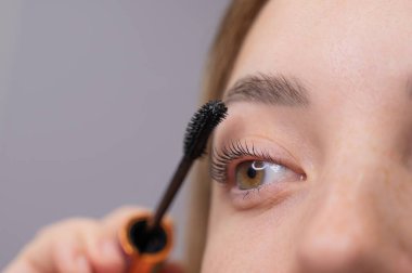 Genç bir kadının dikkatlice maskarasını kirpiklerine sürerken.