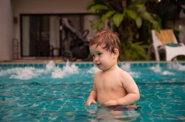 Bir yaşında beyaz çocuk yüzme havuzunda top oynuyor.
