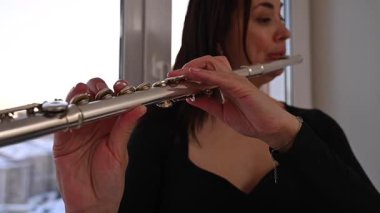 Beyaz kadın pencere eşiğinde flüt çalıyor.