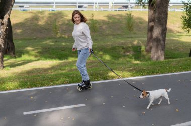 Beyaz kadın, Jack Russell Terrier köpeğiyle parkta paten kayıyor.