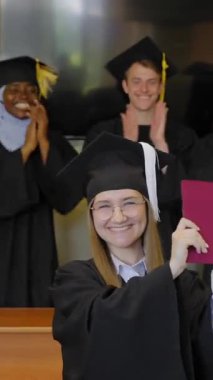 Sınıf arkadaşları onu alkışlarken, elinde diploma tutan beyaz bir kadın.