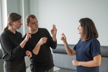 Beyaz kadın erkek ve kadına işaret dili öğretiyor.