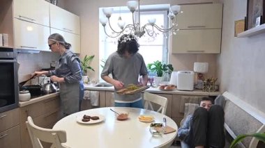 Orta yaşlı beyaz kadın iki oğluyla hamburger pişiriyor.