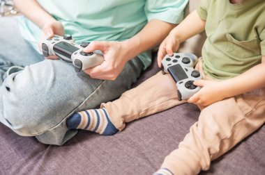 Beyaz kadın küçük oğluna konsol oynamayı öğretiyor. Oyun kolu ellerinde.