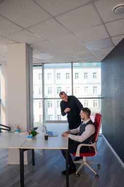 Beyaz adam çalışma masasında durmuş iş hakkında konuşuyor.