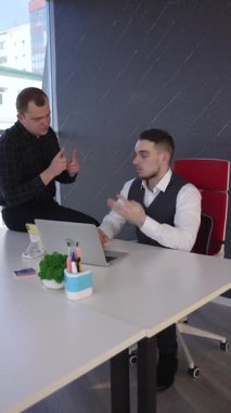 Beyaz adam çalışma masasında durmuş iş hakkında konuşuyor.