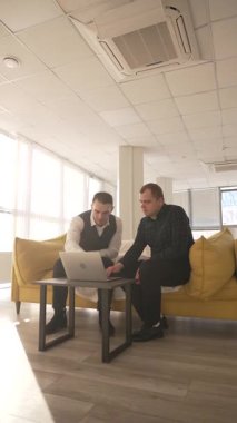 Kanepede otururken laptopta iş tartışan iki beyaz adam. Modern ofis