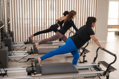 Üç Asyalı kadın bir reformcu üzerinde pilates yapıyor.